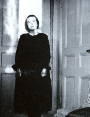 ung Karin Boye står i hörnet av ett rum, framför två dörrar.