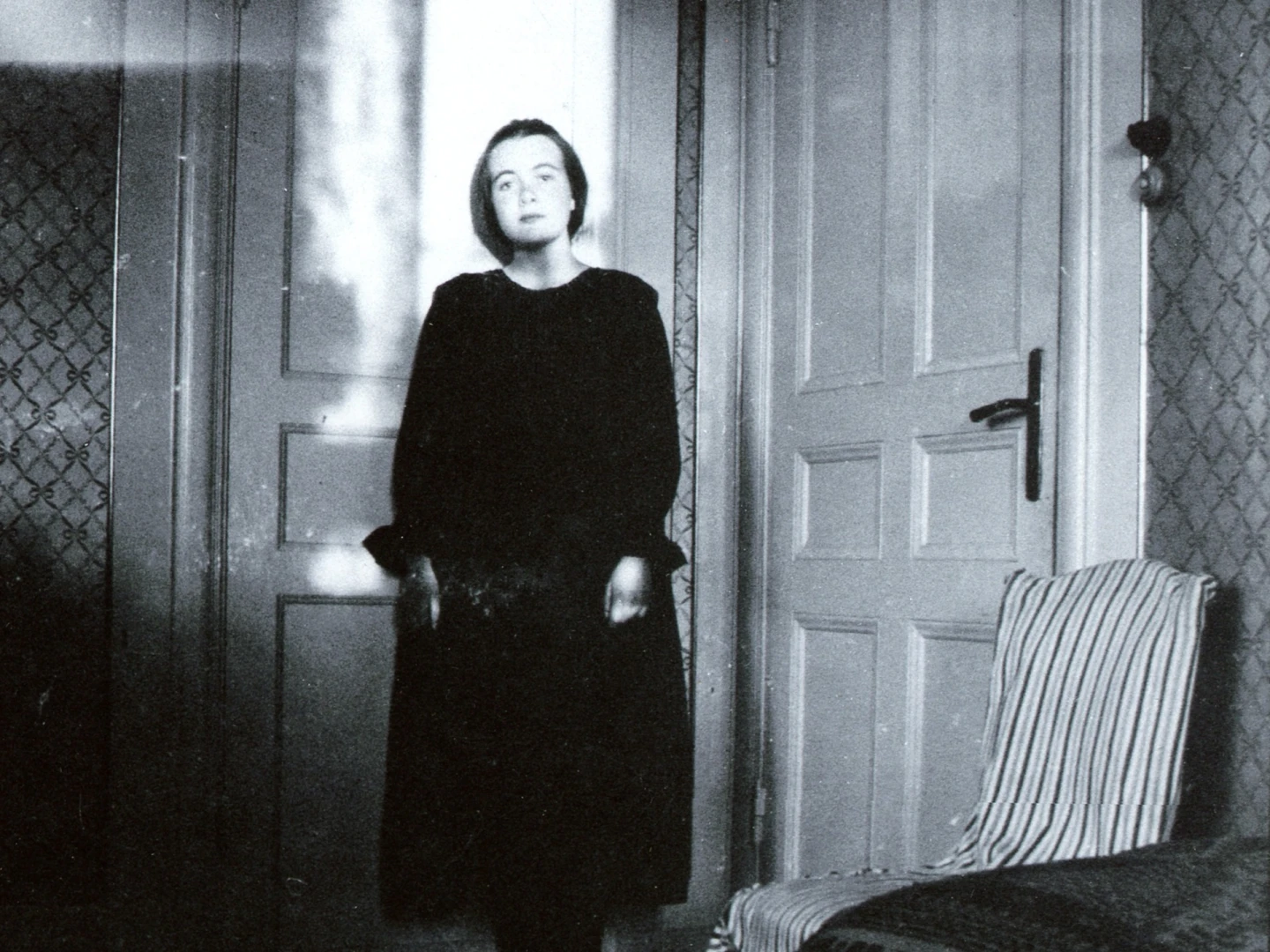 ung Karin Boye står i hörnet av ett rum, framför två dörrar.