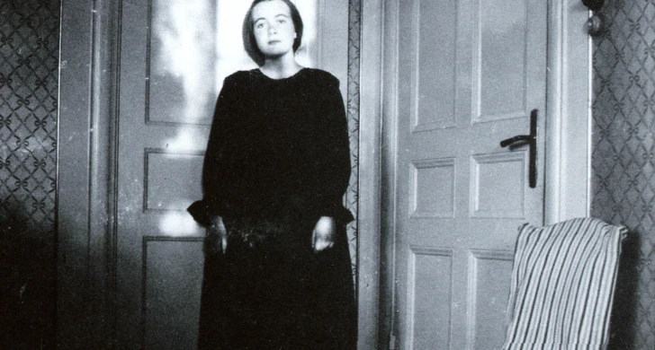 ung Karin Boye står i hörnet av ett rum, framför två dörrar.