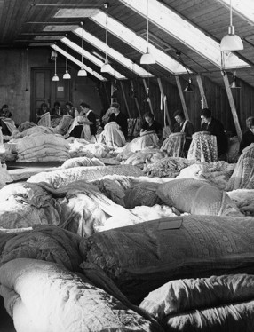 Sömmerskor som sitter och arbetar i en stor sal med ljusinsläpp från taket.