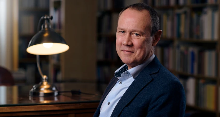 Foto av Bo Eriksson sittande i ett bibliotek med en lampa bredvid.