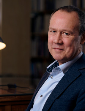 Foto av Bo Eriksson sittande i ett bibliotek med en lampa bredvid.