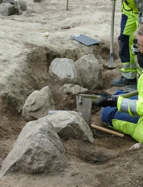 Två arkeologer gräver i ett båtformat hål i marken