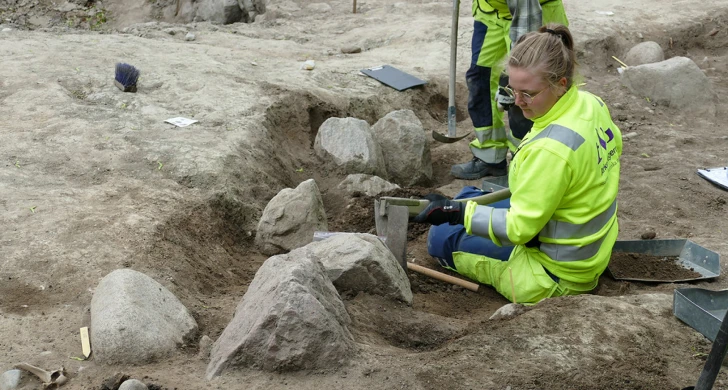 Två arkeologer gräver i ett båtformat hål i marken