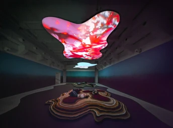 Övergripande vy av två asymmetrisk former i taket där två videofilmer projiceras, personer ligger under dessa på två högar asymmetriska mattor.