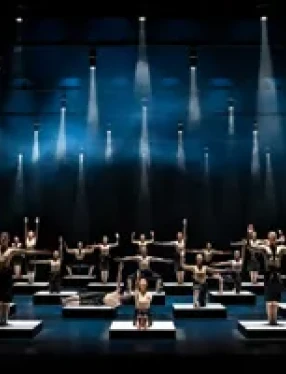 Ett stort antal dansare är placerade på kuber på scengolvet - ovan dem spotlights.