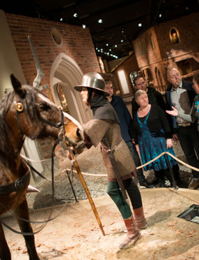 En guide visar en medeltida riddare till häst för en grupp.