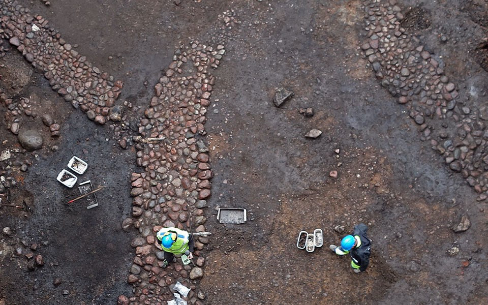 Två arkeologer står vid fynd av stenbelagd medeltida gata från 1300-talet.