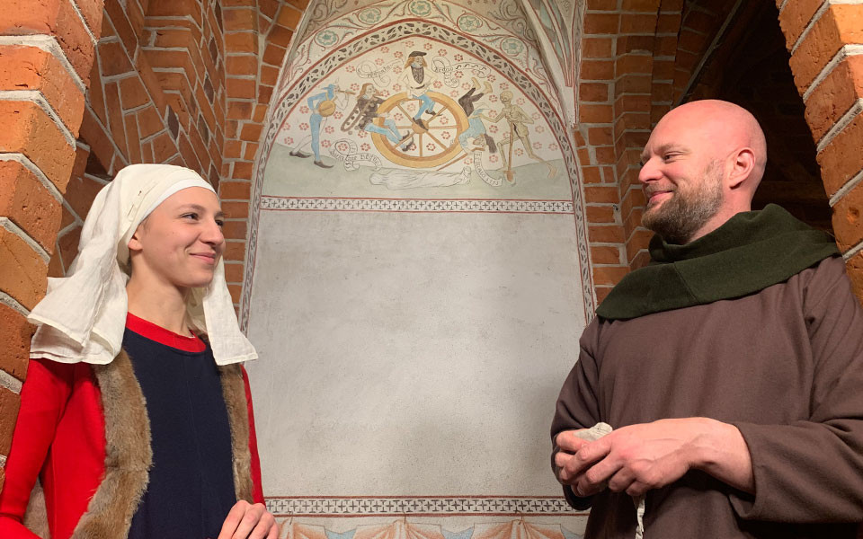 En man och en kvinna i medeltida kläder i en medeltida kyrkobyggnad.