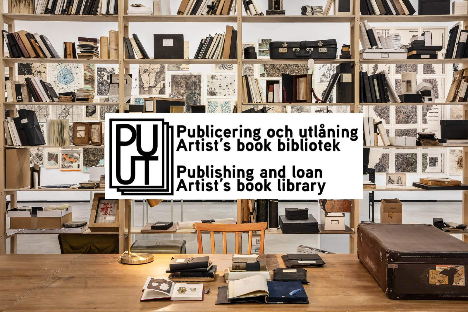 Ett skrivbord med en bokhylla bakom. En stor logotyp mitt i bild.